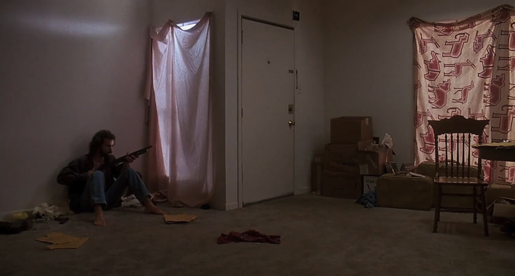 Jim seduto a terra con un fucile in una scena di Effetto allucinante (1991).